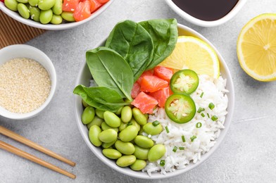 Photo of Poke bowl with salmon, edamame beans and rice on light grey table, flat lay