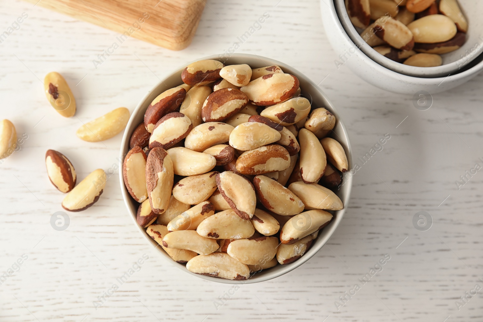 Photo of Bowls with tasty Brazil nuts on white wooden table, top view