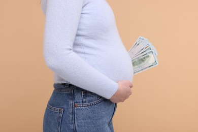 Photo of Surrogate mother. Pregnant woman with dollar banknotes on beige background, closeup