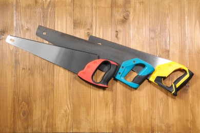 Photo of Saws with colorful handles on wooden background, flat lay