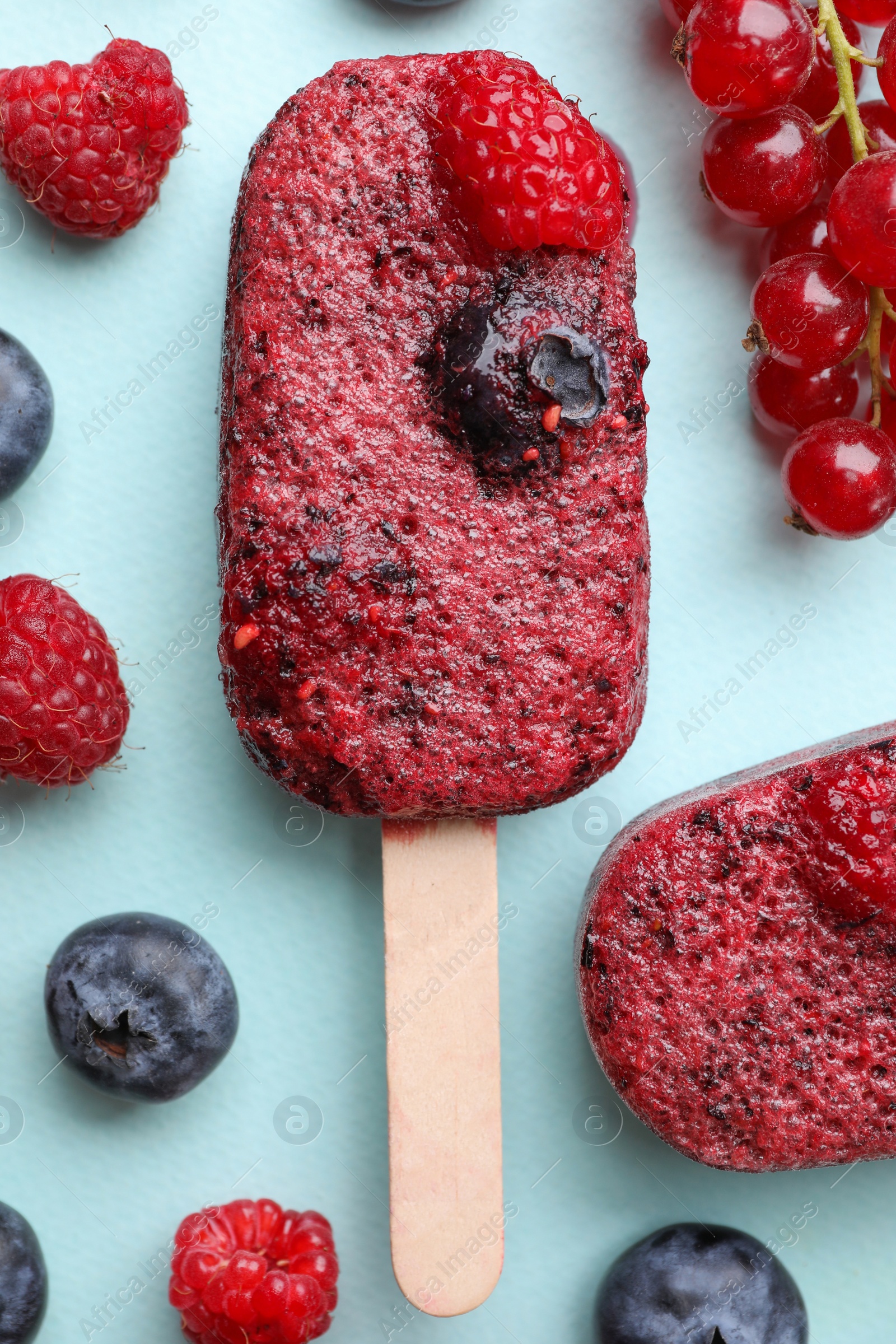 Photo of Tasty berry ice pops on light blue background, flat lay. Fruit popsicle