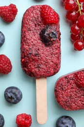 Photo of Tasty berry ice pops on light blue background, flat lay. Fruit popsicle