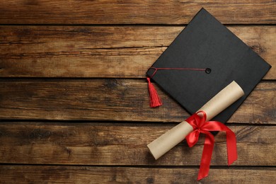 Photo of Graduation hat and diploma on wooden table, flat lay. Space for text