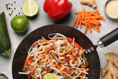 Photo of Shrimp stir fry with noodles and vegetables in wok surrounded by ingredients on grey table, flat lay