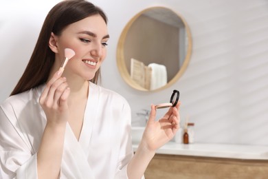 Photo of Beautiful young woman applying blusher with brush indoors. Space for text