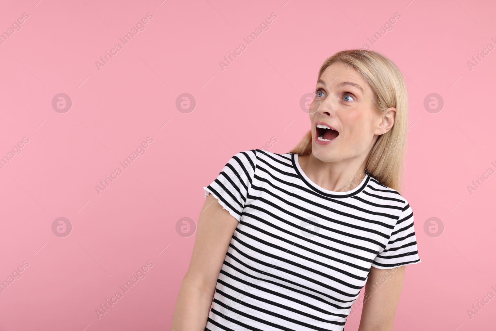 Photo of Portrait of surprised woman on pink background, space for text