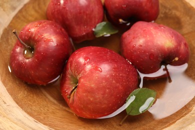 Photo of Fresh red apples and leaves in wooden bowl with water, closeup