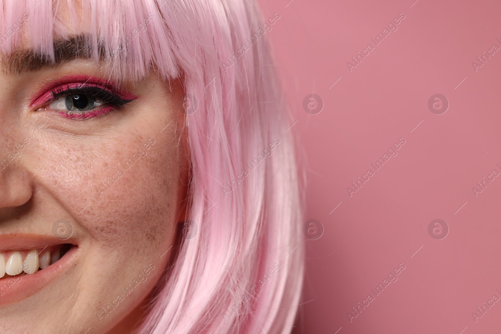 Photo of Smiling woman with bright makeup and fake freckles on pink background, closeup. Space for text