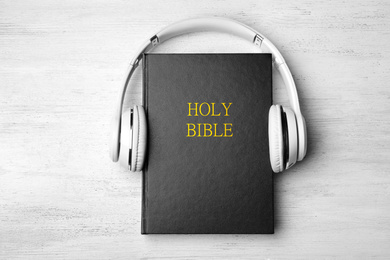 Photo of Bible and headphones on white wooden background, top view. Religious audiobook