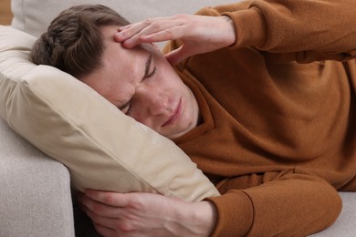 Sad man suffering from headache on sofa indoors