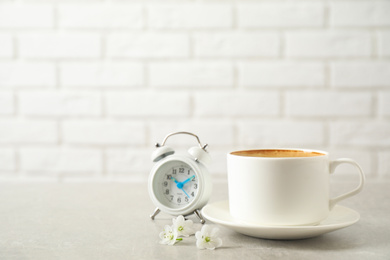 Cup of morning coffee, flowers and alarm clock on light grey table. Space for text
