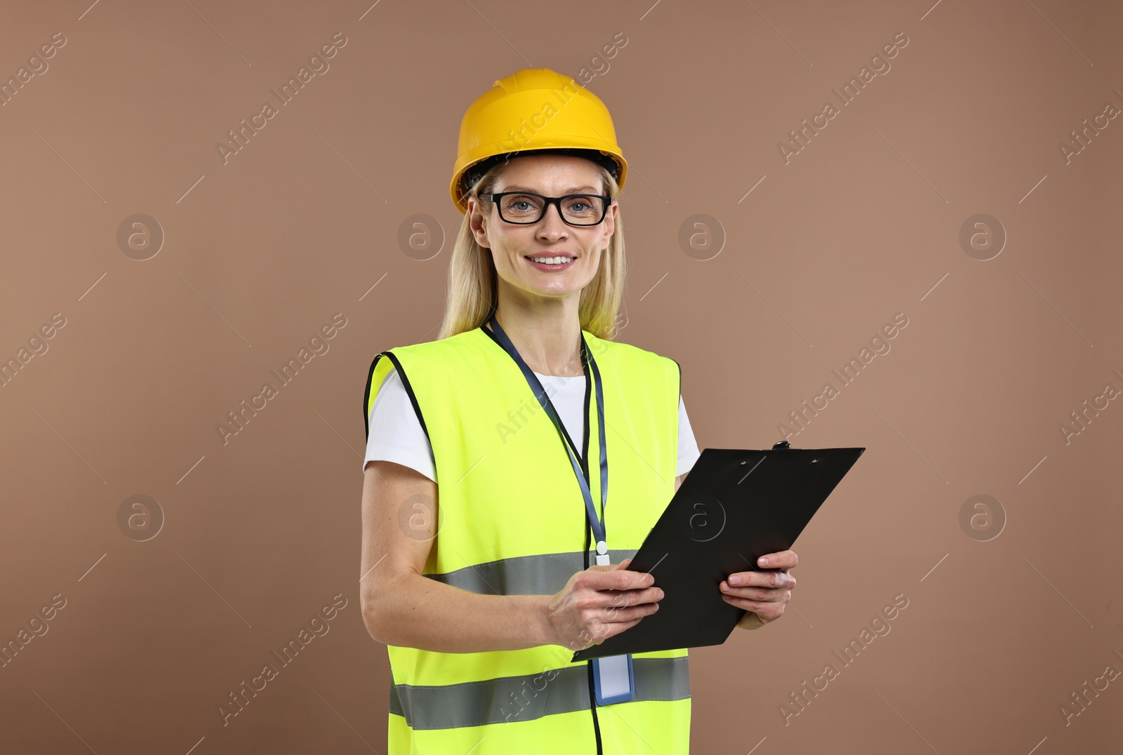 Photo of Engineer in hard hat holding clipboard on brown background