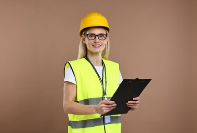 Engineer in hard hat holding clipboard on brown background