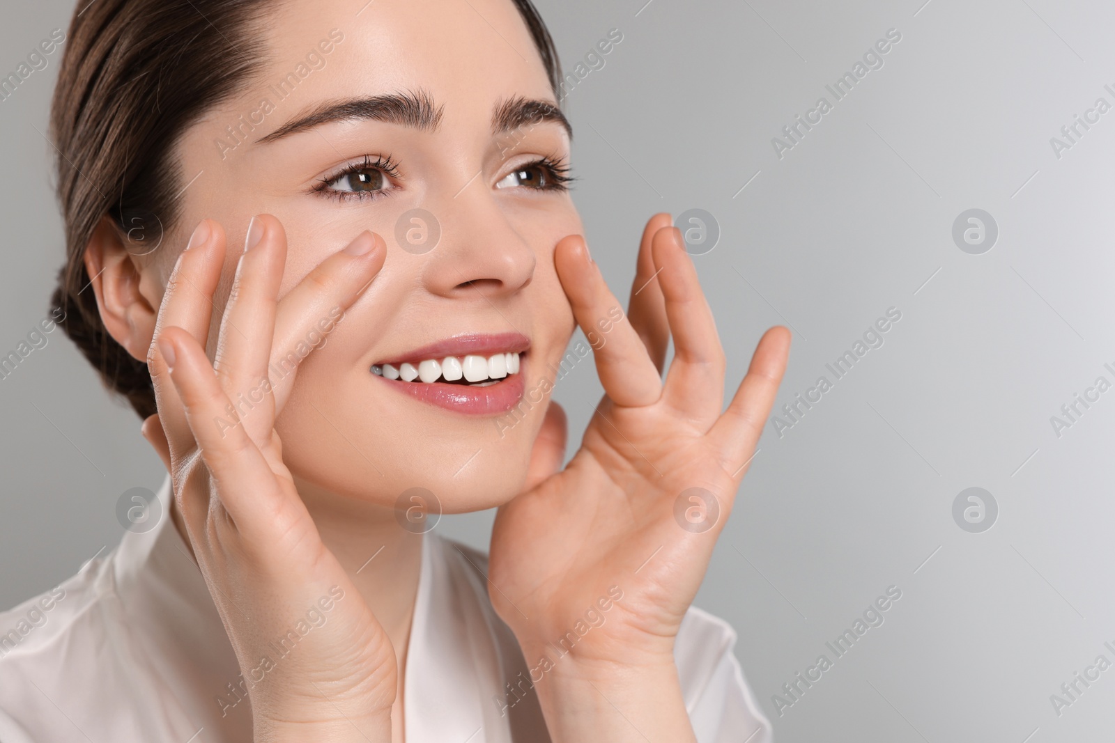 Photo of Young woman massaging her face on grey background. Space for text