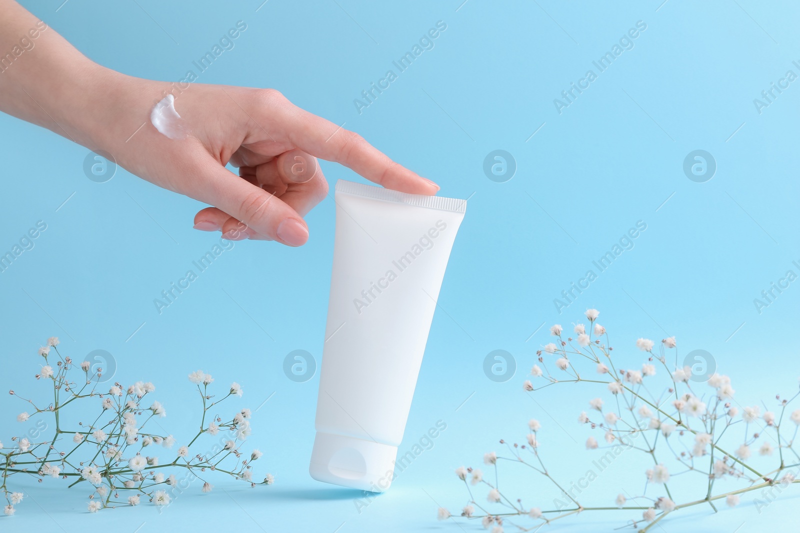 Photo of Woman with tube of cream and flowers on light blue background, closeup