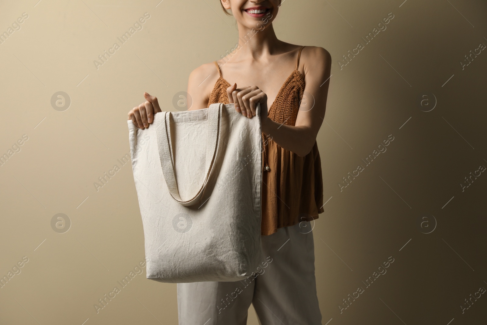 Photo of Happy young woman with blank eco friendly bag against beige background, closeup