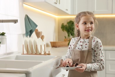Photo of Little girl wiping plate with towel in kitchen