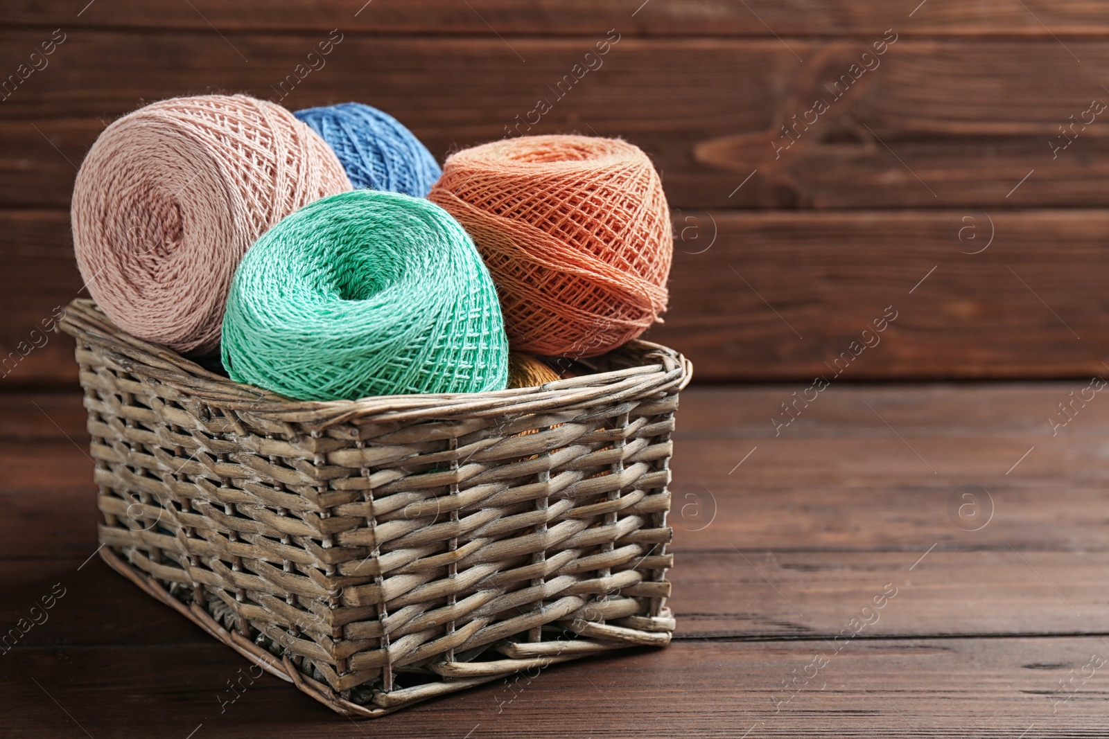 Photo of Colorful clews of threads in wicker basket on table against wooden background. Space for text