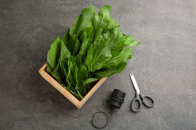 Photo of Fresh green sorrel leaves in crate, scissors and thread on grey table, flat lay