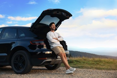 Photo of Happy man sitting in trunk of modern car on roadside outdoors