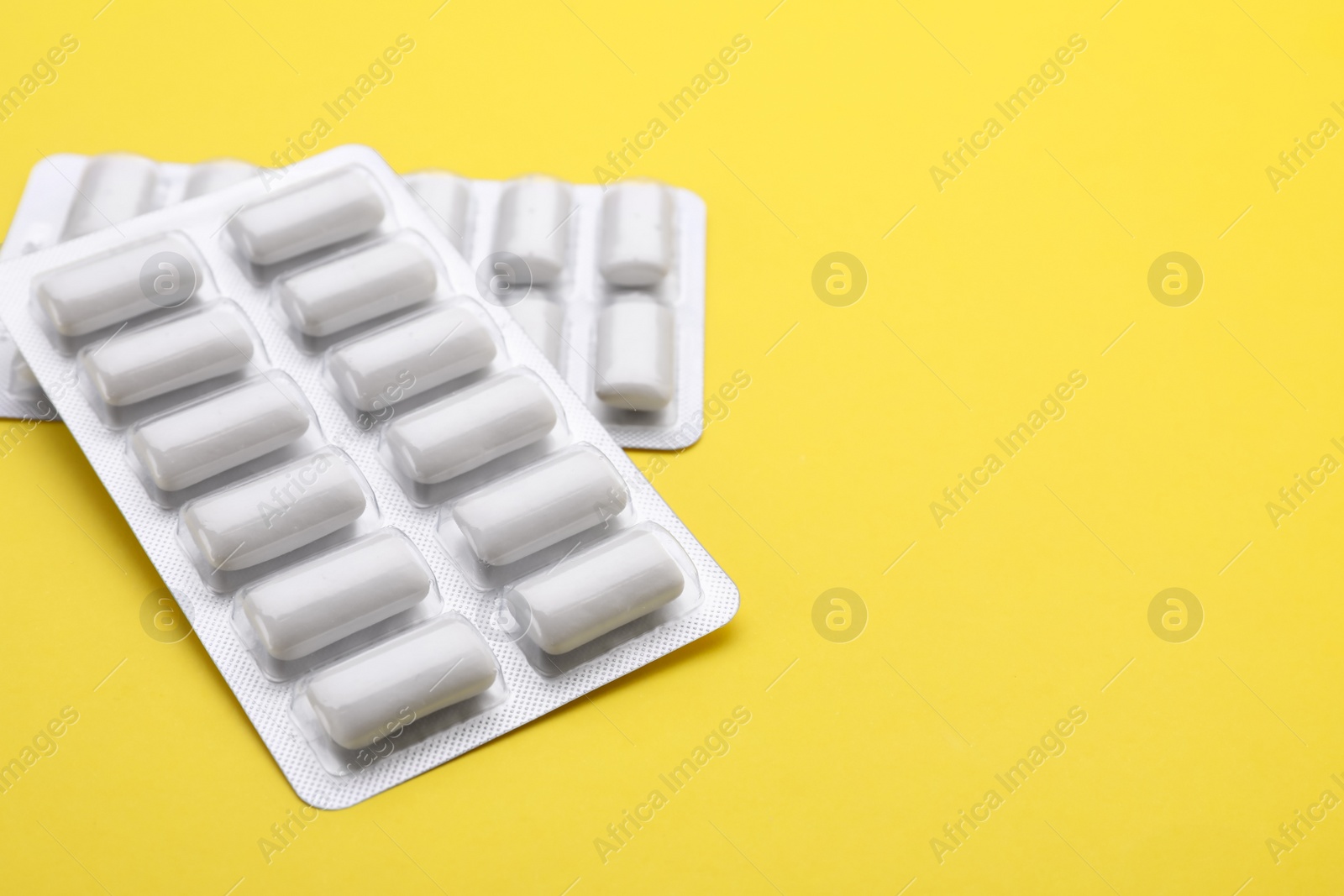 Photo of Blisters with chewing gums on yellow background, closeup. Space for text