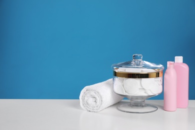 Photo of Jar with cotton pads on white table against blue background. Space for text