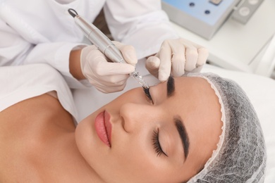 Photo of Young woman undergoing procedure of permanent eye makeup in tattoo salon, closeup