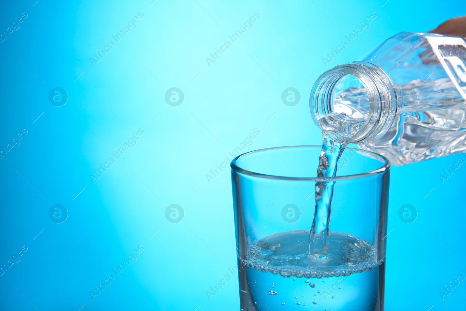 Photo of Pouring water from bottle into glass on blue background. Space for text