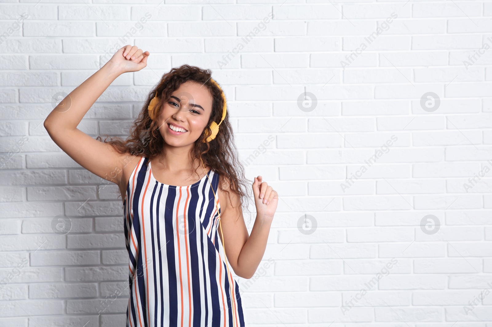 Photo of African-American woman listening to music with headphones near brick wall, space for text