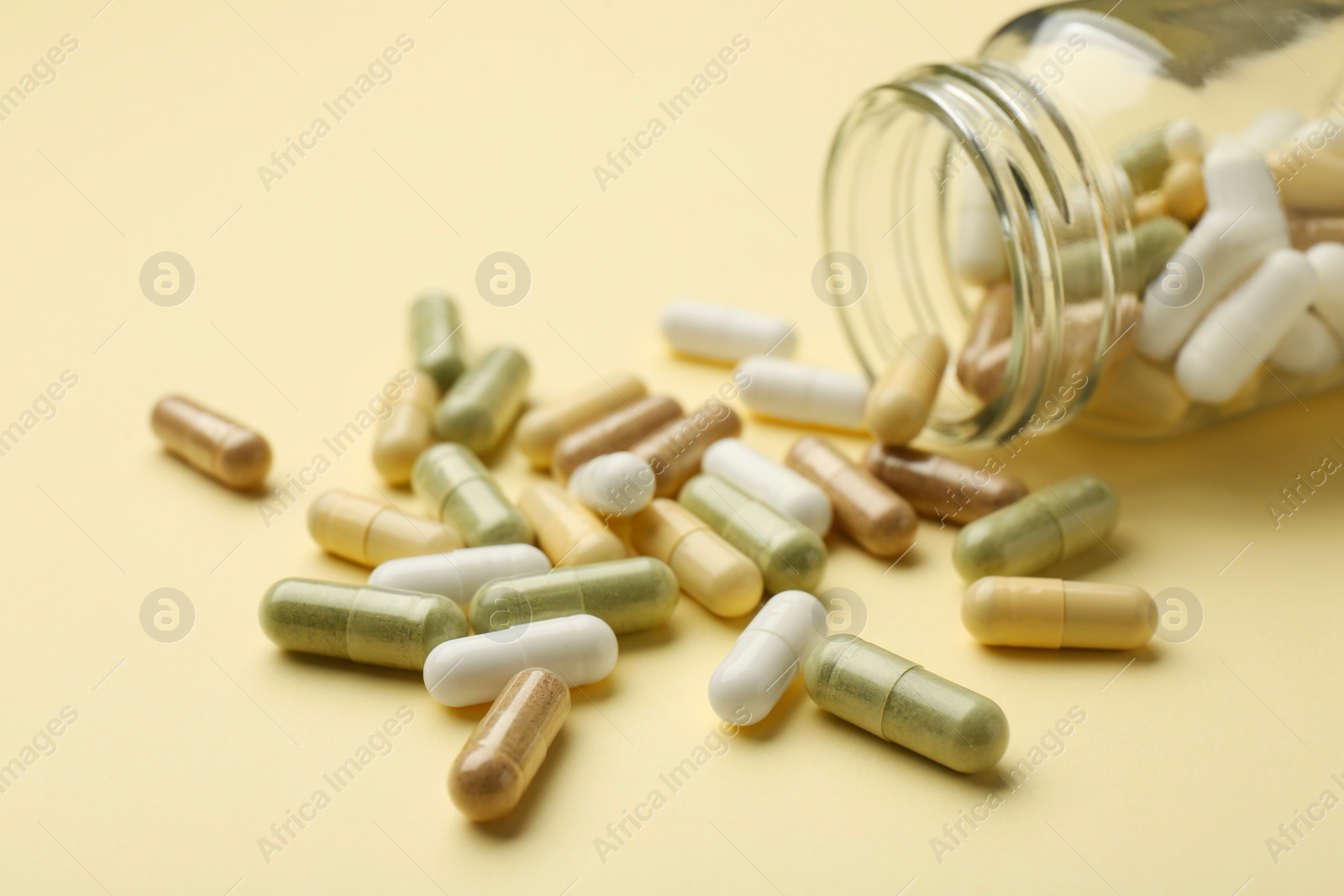 Photo of Vitamin pills and bottle on beige background, closeup