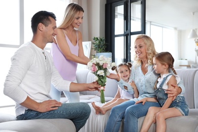 Photo of Happy family with little children congratulating mature woman in living room