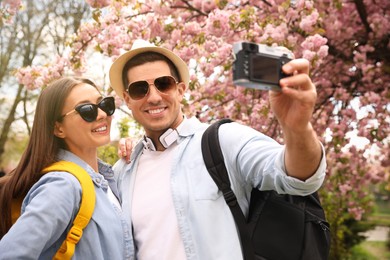 Happy couple taking selfie near blossoming sakura outdoors on spring day