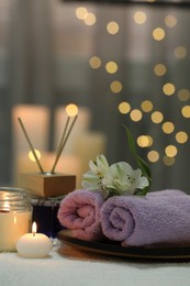 Beautiful composition with different spa products and flowers on white towel against blurred lights