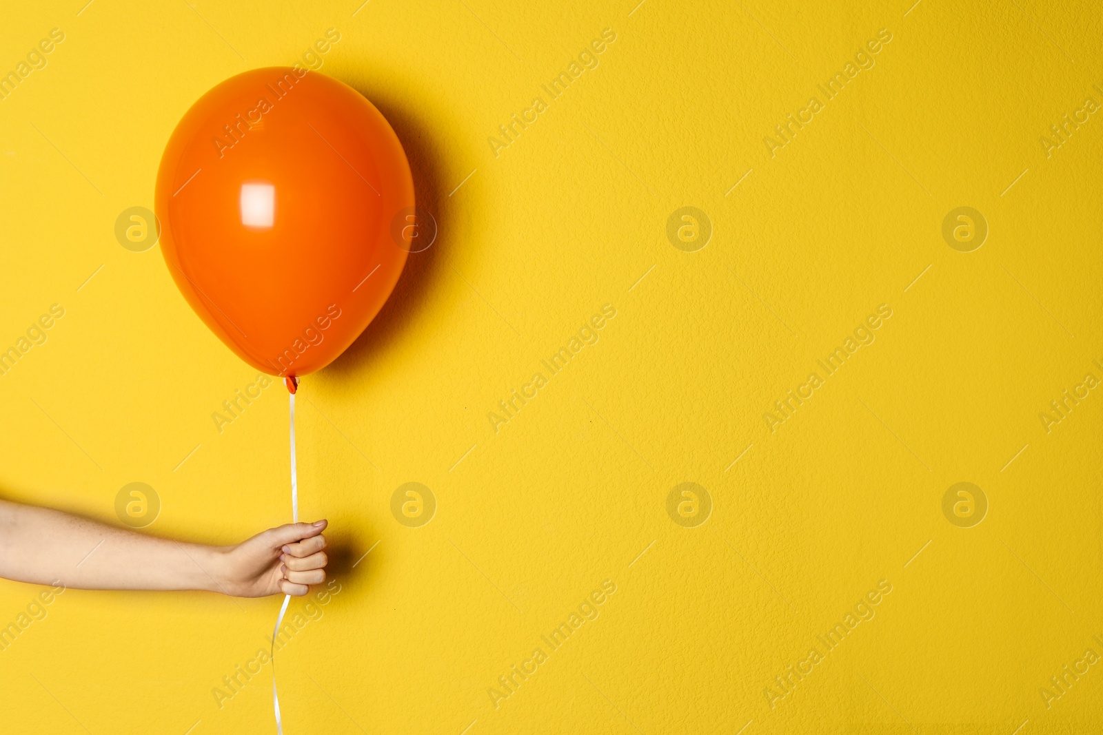 Photo of Woman holding orange balloon on color background