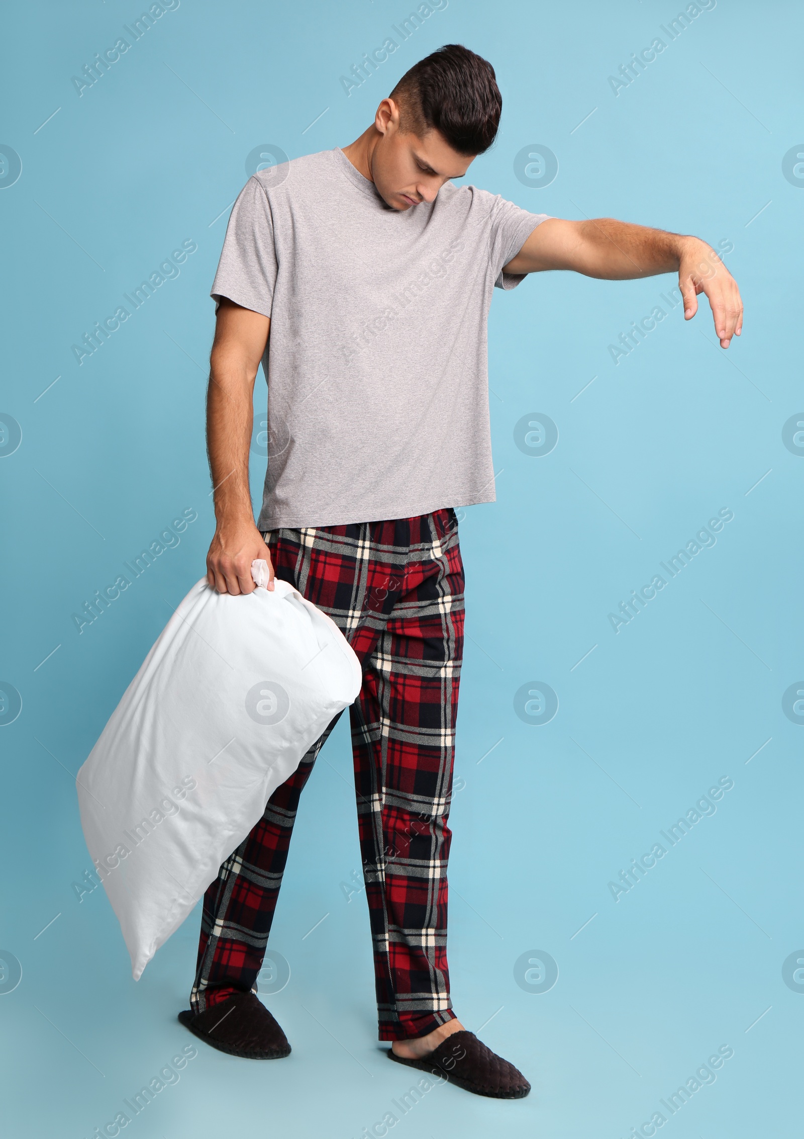 Photo of Somnambulist with soft pillow on light blue background. Sleepwalking