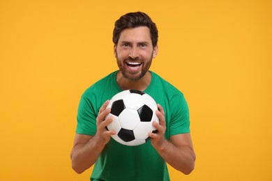 Emotional sports fan with soccer ball on orange background