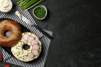 Photo of Delicious bagel with cream cheese, green onion and radish on black table, flat lay. Space for text