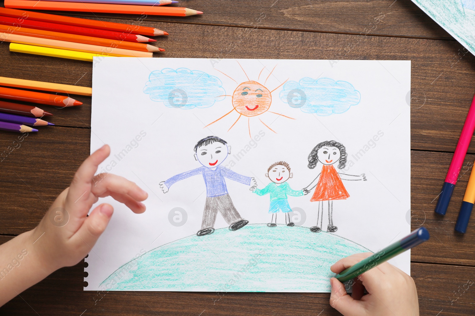 Photo of Little boy drawing with pencil at wooden table, top view. Child`s art