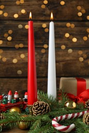 Burning candles and festive decor on wooden table, bokeh effect. Christmas eve