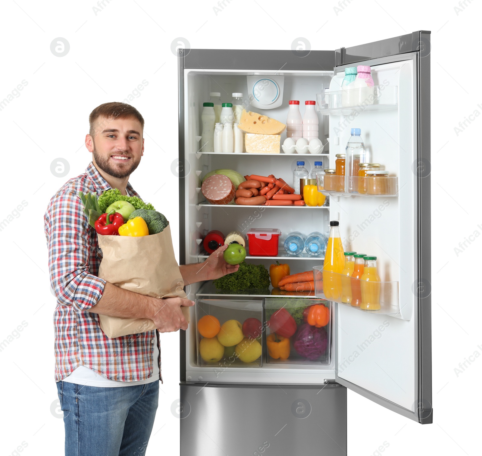 Photo of Young man with bag of groceries and apple near open refrigerator on white background