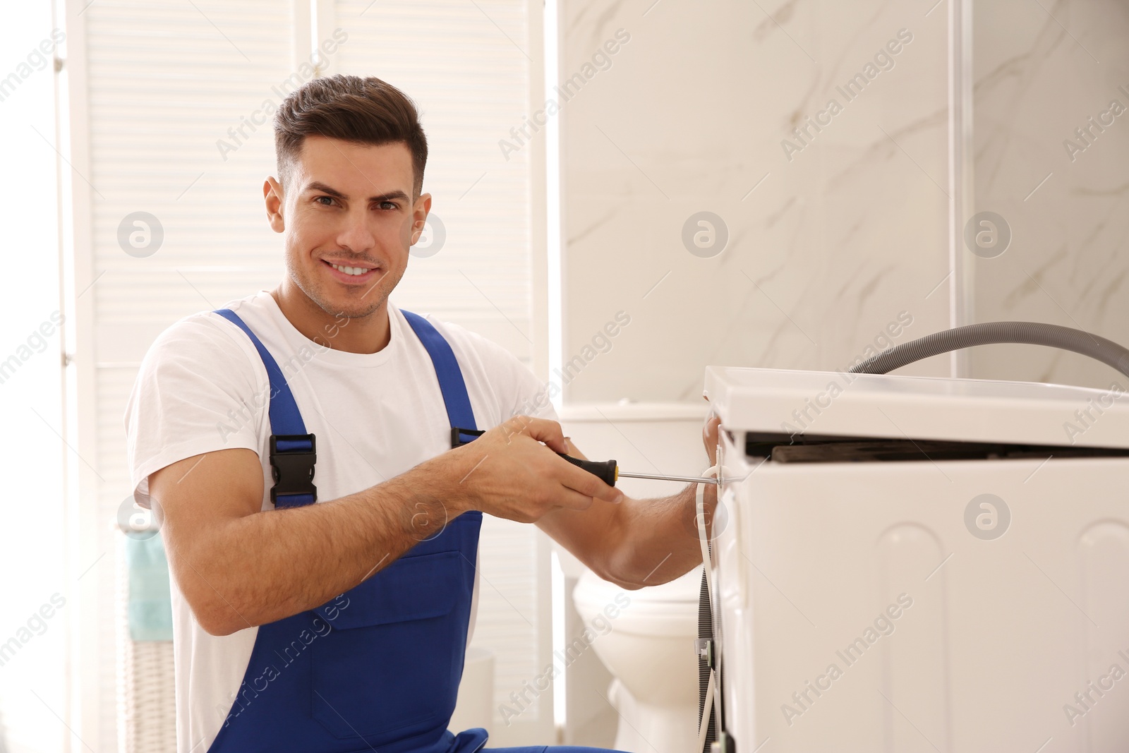 Photo of Professional plumber repairing washing machine in bathroom