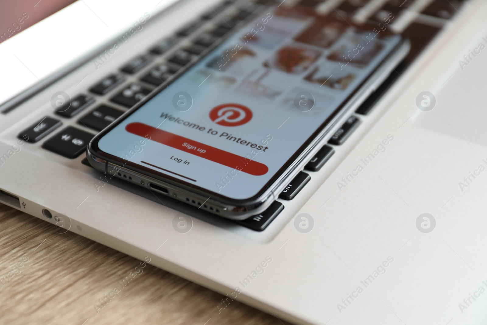 Photo of MYKOLAIV, UKRAINE - AUGUST 28, 2020: iPhone 11 displaying Pinterest app and MacBook laptop on wooden table, closeup