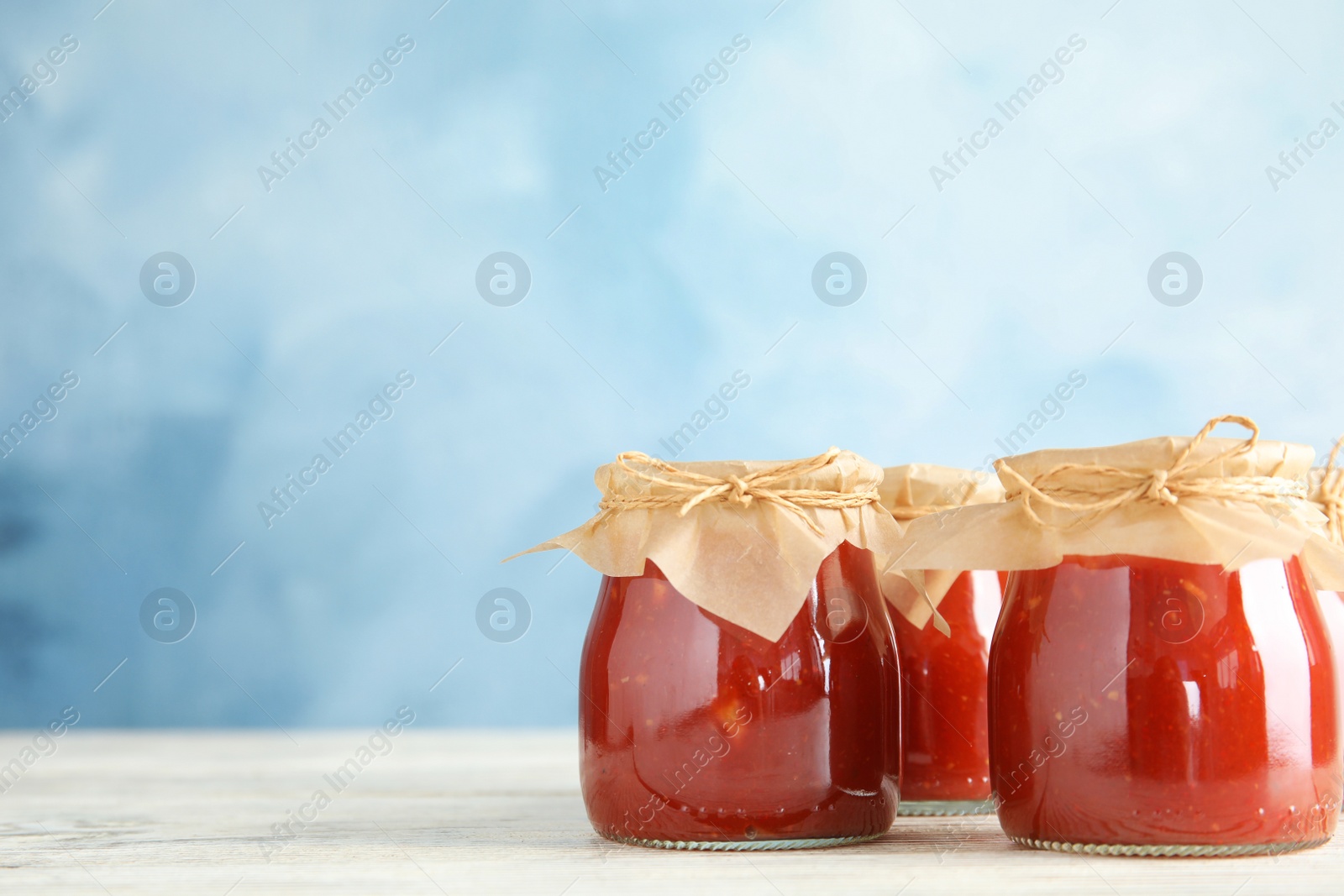 Photo of Jars of tomato sauce on wooden table against color background, space for text