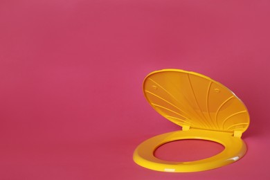 Photo of New yellow plastic toilet seat on pink background, space for text