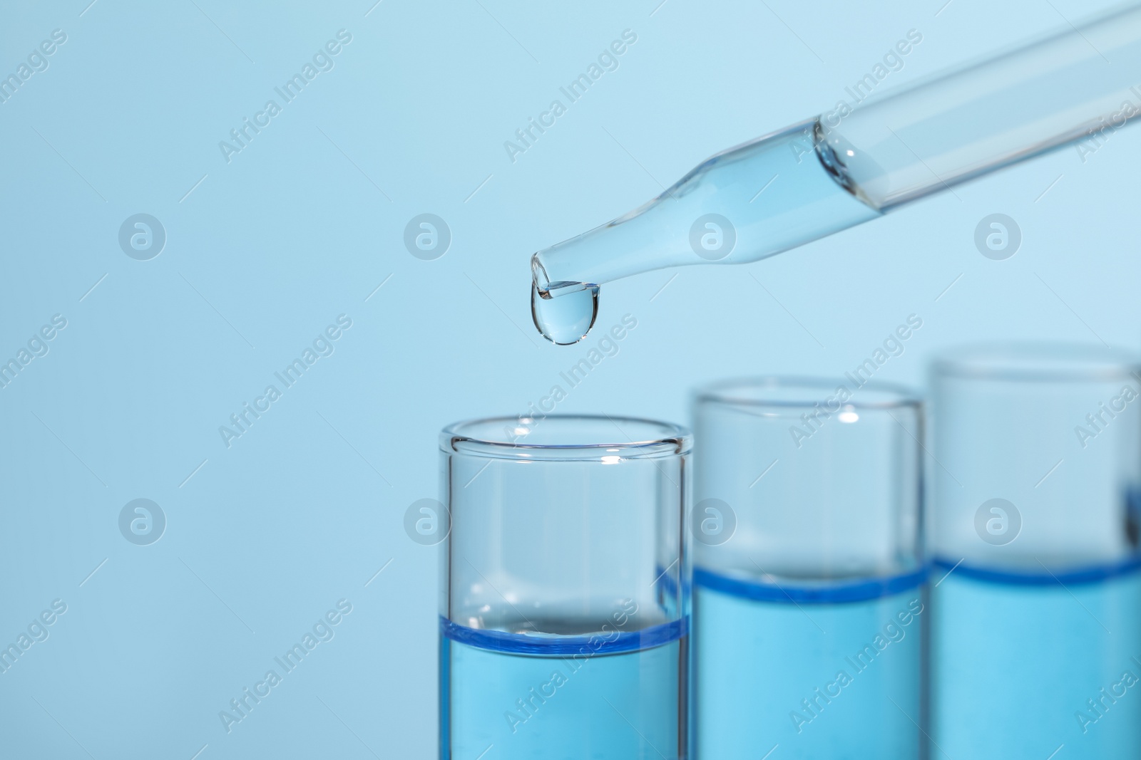 Photo of Dripping reagent into test tube on light blue background, closeup. Laboratory analysis