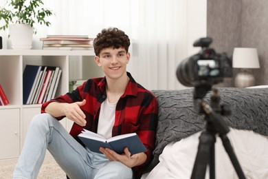 Smiling teenage blogger reading book while streaming at home