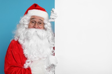 Photo of Santa Claus holding blank poster on light blue background, space for text