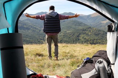 Man in mountains on sunny day, view from camping tent