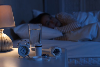 Photo of Woman suffering from insomnia in bed at night, focus on nightstand with pills, alarm clock and water