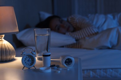 Woman suffering from insomnia in bed at night, focus on nightstand with pills, alarm clock and water